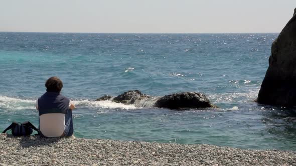 Young Man Sitting on Seaside and Looking at the Sea and Then Goes Away