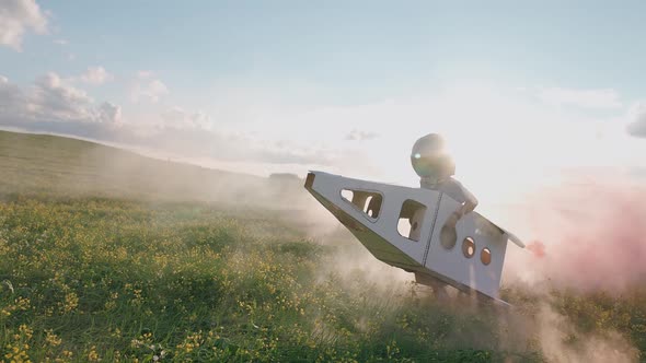 Countryside Boy Plays in an Astronaut Helmet in Nature with a Cardboard Model of a Space Shuttle a