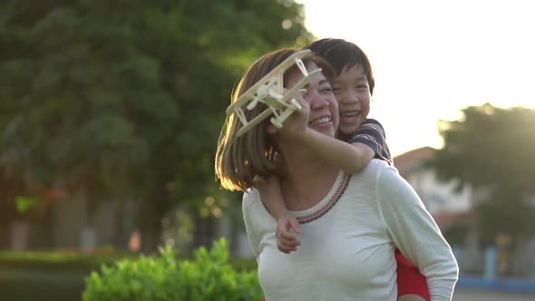 Cute Asian Mother And Son Playing Wooden Airplane Together In The Park Outdoors 