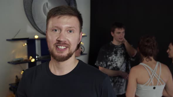 Young Beard Guy Waving to the Camera While People are Chatting at the Background