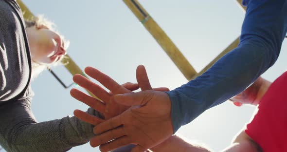 Happy, fit diverse group making hand stack and cheering in the sun after obstacle course