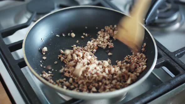 Woman stirring chopped nuts in pan on stovetop