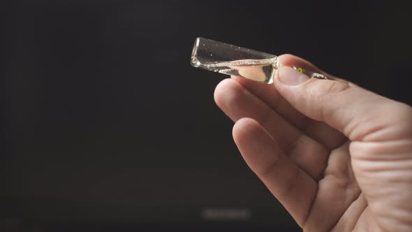 Close-up of a Man's Hand on a Dark Background Holding an Ampoule for Injection. Coronavirus