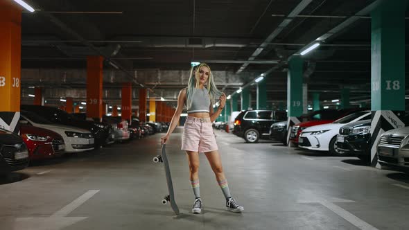 Young Woman with Bright Unusual Appearance Posing with Skateboard at Underground Parking Zone