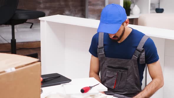 Close Up of Young Man in Coverall Using Laptop To Assembly Furniture