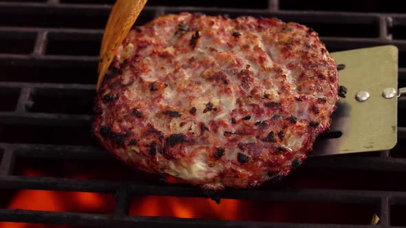 Closeup of the Appetizing Burger Cutlet with Onions Flipping Above the Fire