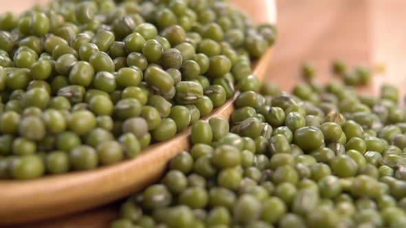 A full wooden spoon of green uncooked mung beans. Falling dry legumes in slow motion