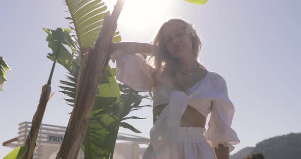 Blonde girl enjoying summer and hiding from the sun in palm leaves. Vacation hotel resort.