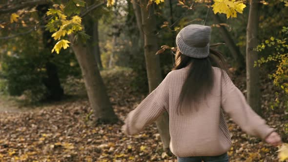 Stylish Girl Walks and Whirls in Park with Autumn Leaf in Hand