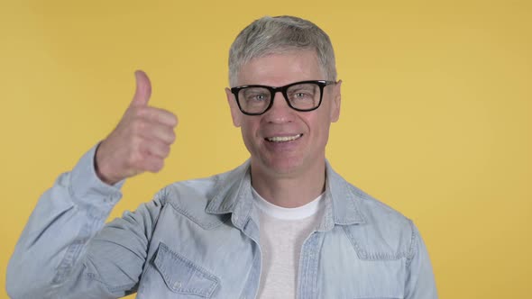 Casual Senior Man Gesturing Thumbs Up on Yellow Background