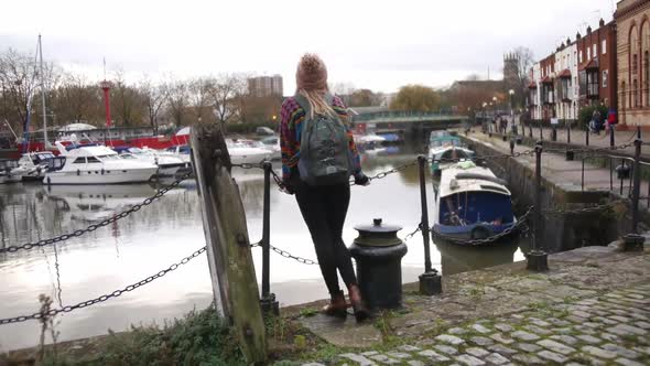 woman smiling into the camera and then starts looking at the waterside of Bristol harbour.