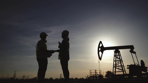 Silhouette Two Engineers Shaking Hands on the Background a Oil Pump at Sunset. Industrial, Oil