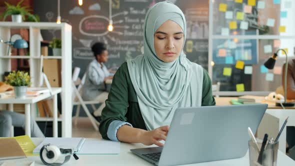 Portrait of Successful Muslim Woman in Hijab Working with Laptop Typing at Desk