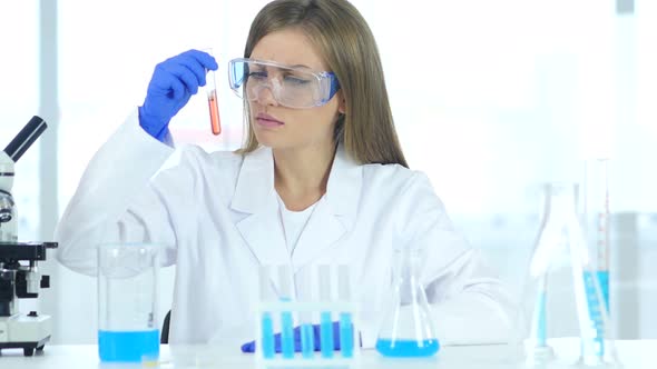 Female Scientist Looking at Red Solution in Test Tube in Laboratory