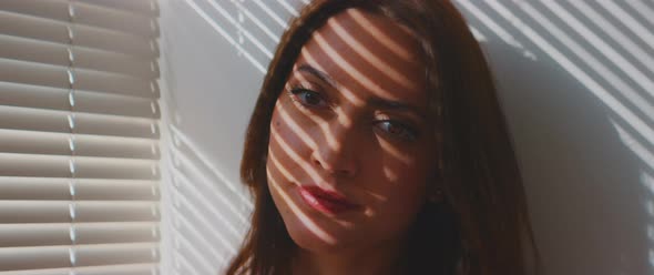 Young woman looking into the camera shadow of shutters covers her face