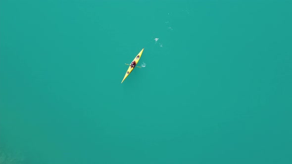 Woman kayaking through clean vibrant green glacier water in yellow kayak - Static birdseye aerial vi