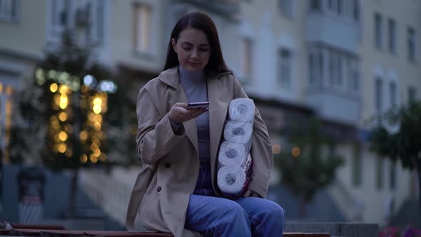 Woman Sits on Bench in Medical Mask with Toilet Paper and Smartphone During the Second Wave