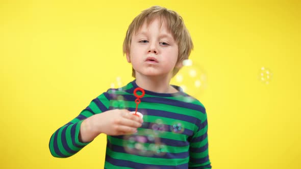 Portrait of Happy Relaxed Boy Blowing Soap Bubbles at Yellow Background