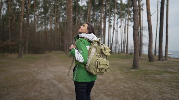 Live Camera Follows Caucasian Woman with Rucksack Strolling in Spring Autumn Forest Looking Around