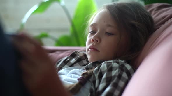 Closeup of Adorable Caucasian Child Girl Lying on Bed Reading Interest Book and Flipping Pages