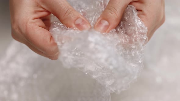 Female Hands Burst Air Bubbles on Bubble Wrap on a White Background