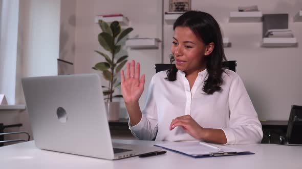 Businesswoman Waving in Front of Laptop Screen and Talking at Table in Modern Office Spbi