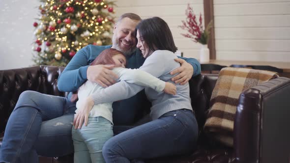 Happy Mid-adult Caucasian Parents Hugging Little Daughter on New Year's Eve. Wide Shot Portrait of