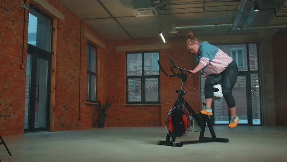 Athletic Woman Riding on Spinning Stationary Bike Training Routine in Haze Gym Weight Loss Indoors