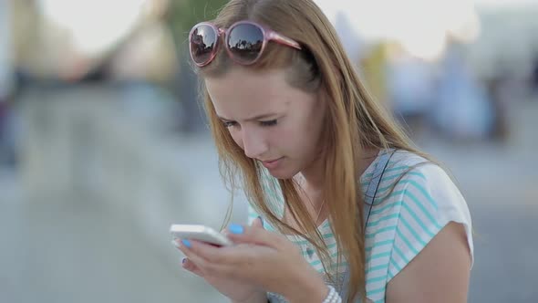 Girl Seriously Using a Smart Phone in a City Embankment Sitting