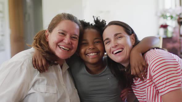 Portrait of happy caucasian lesbian couple and their african american daughter embracing and smiling