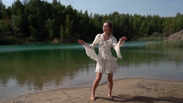Cute Blonde Woman in White Dress Enjoying Nature, Dancing Barefoot on the Lake Shore. Attractive