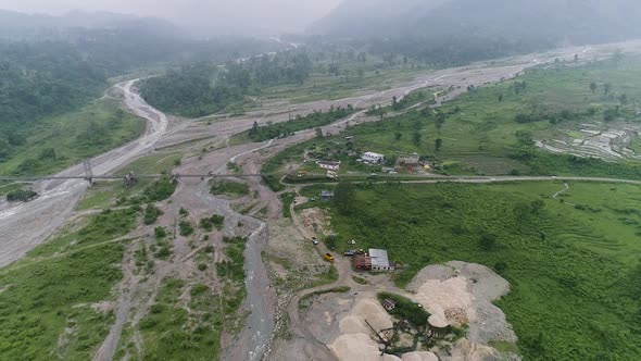 Bridge over river runs through the valleys with lush vegetation surrounded by mountains hidden by fo