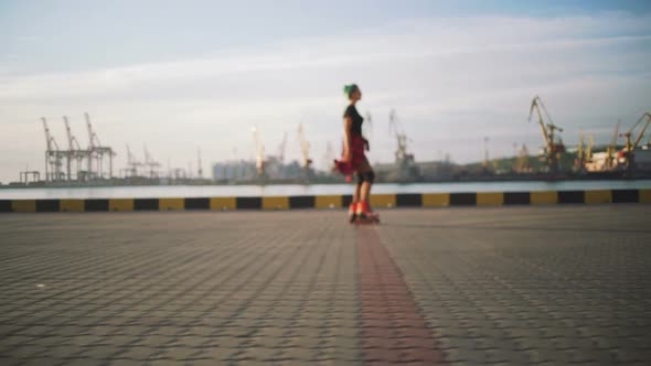 Young Stylish Funky Girl with Green Hair Riding Roller Skates and Dancing Near Sea Port During