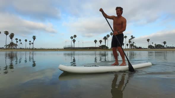 Tracking view of a man paddling his SUP stand-up paddleboard in a lake