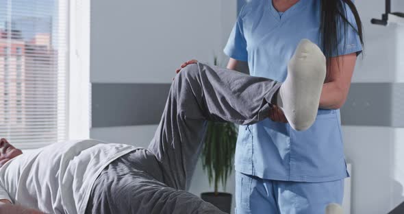 Female Doctor Stretching Leg of Aged Patient and Talking