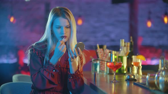 Gorgeous Young Blonde Woman Sitting By the Bartender Stand and Applying Red Lipstick on Her Lips