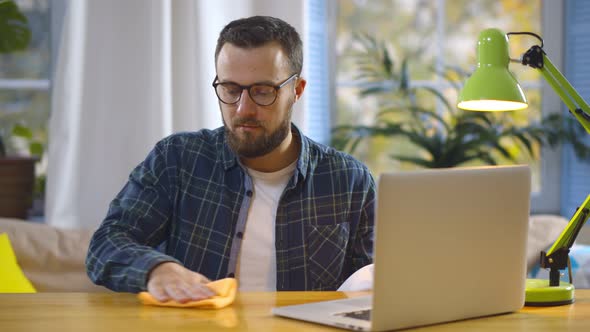 Young Man Cleaning Desktop with Detergent Sprayer and Cloth Before Start Working at Home Office