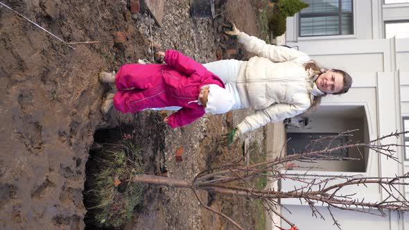 Happy Smiling Woman Plants Apple Tree with Her Little Daughter in Garden on Sunny Autumn Day