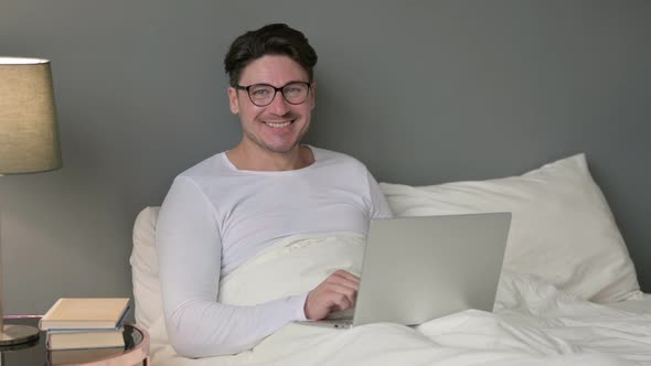 Middle Aged Man with Laptop Smiling at Camera in Bed 