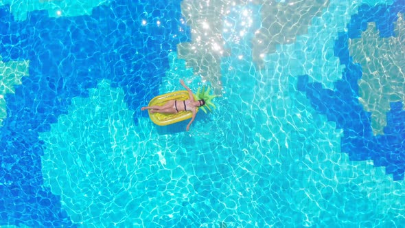 One Woman Rests in a Blue Pool, Floating on a Mattress