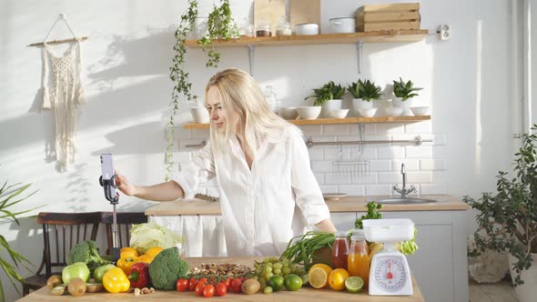 Pretty Blonde Writes a Video Blog About Healthy Eating on Her Mobile Phone Standing at Home in the