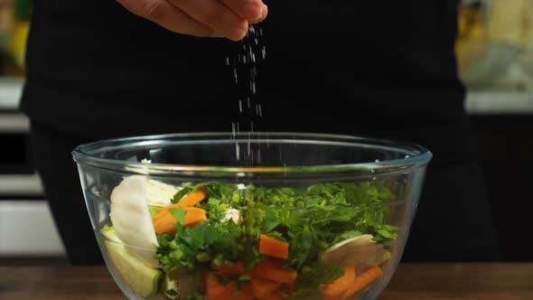 Closeup of a Woman's Hand Sprinkling Salt on a Salad in a Glass Bowl