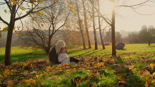 Mother and daughter watching tablet at picnic in autumn park outdoors. Two females sitting on plaid