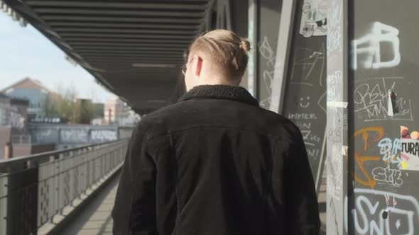 Young European Man with Man Bun, Glasses and a Black Jacket Walking on Sidewalk during Daytime in Ha