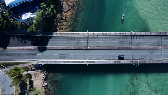 Fishing boating under an ocean estuary bridge while cars and pedestrians travel over from above. Dro