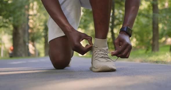 Unrecognizable Sportsman Tying Shoelaces on Jogging Track in Park, Closeup