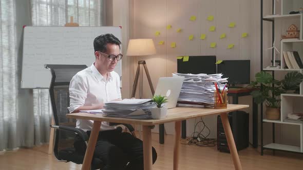 Asian Man Having Video Call On Laptop While Working With Documents At The Office