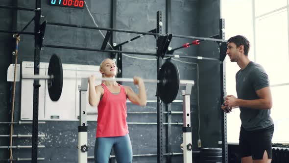 Muscular Girl Lifting Heavy Barbell Under Trainer's Guidance in Modern Gym