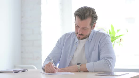 Young Man Writing on Paper in Office