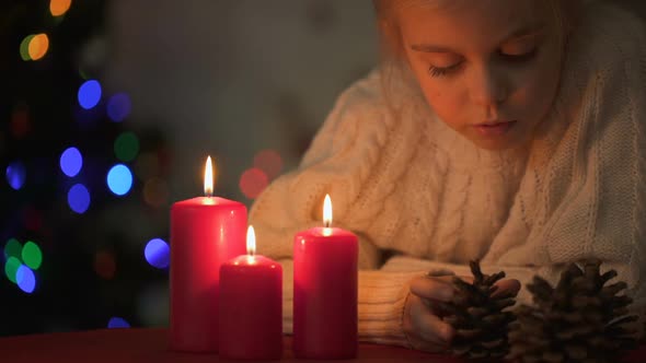 Adorable Girl Playing With Pine Cone Near Burning Candles, Christmas Time